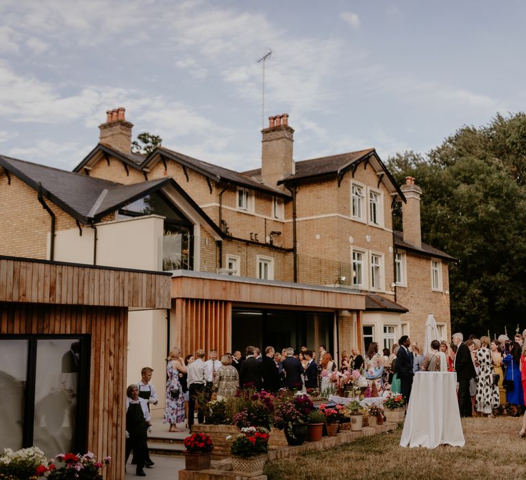 Wedding guests stand outside house for back garden wedding with bright florals 