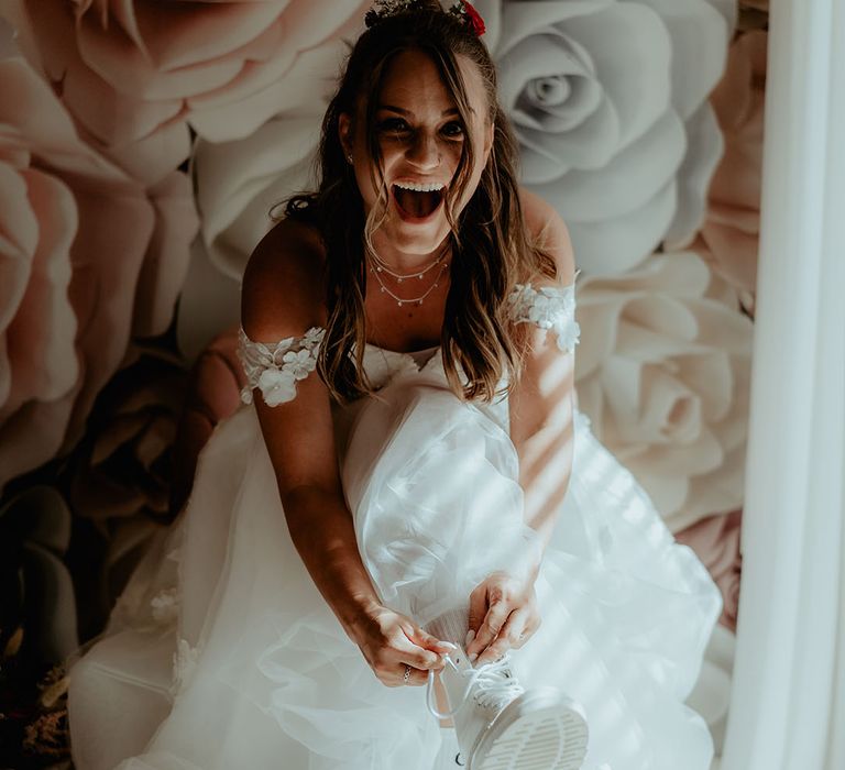 Bride in a flower off the shoulder tulle wedding dress putting on Doc Martens for rustic barn wedding 