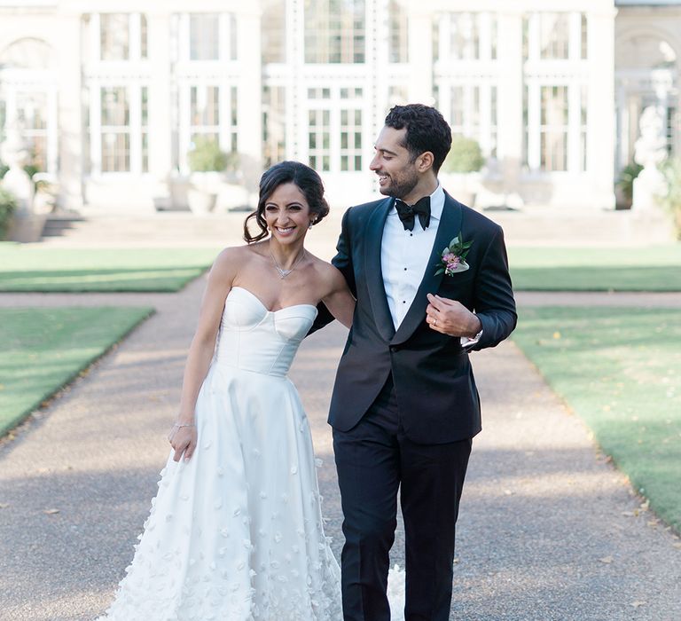 Bride in bespoke Emma Beaumont wedding dress walks alongside her groom in black-tie 