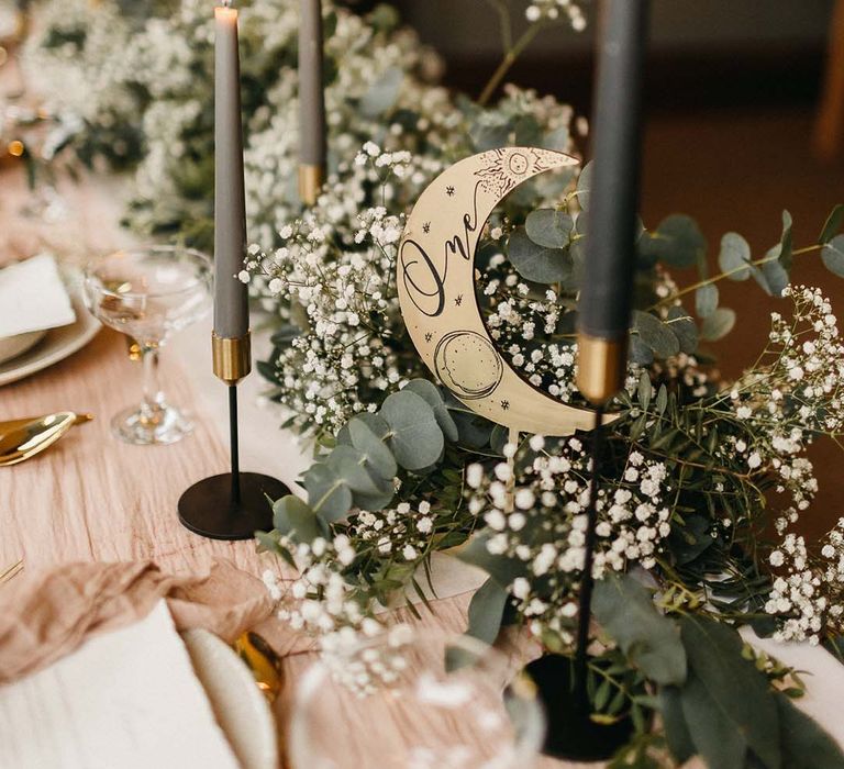 Handmade golden moon table decorations with sage green candles and light pink table runners with foliage and baby's-breath decorations