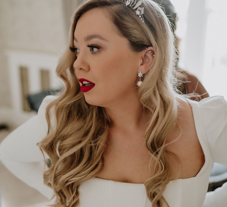 Bride in square neck long sleeve satin wedding dress with, pearl earrings, pearl encrusted industrial earring and bridal crown holding her two tier veil