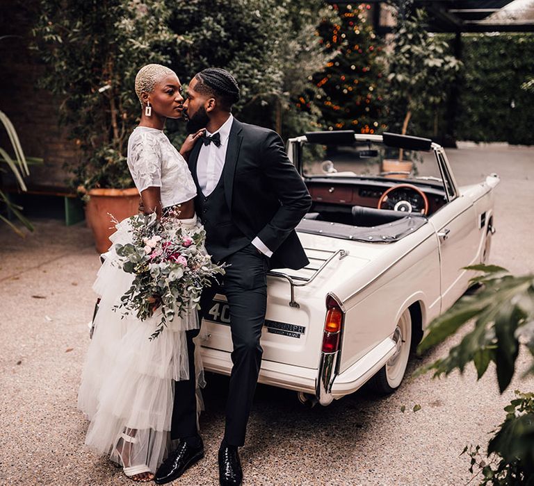 Bride and Groom pose in front of a classic vintage wedding car and greenery at London wedding venue, 100 Barrington