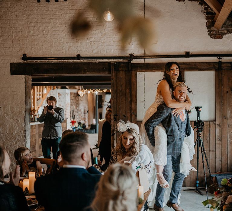 The groom in a three piece grey checkered suit and orange tie stands with the bride piggybacking 