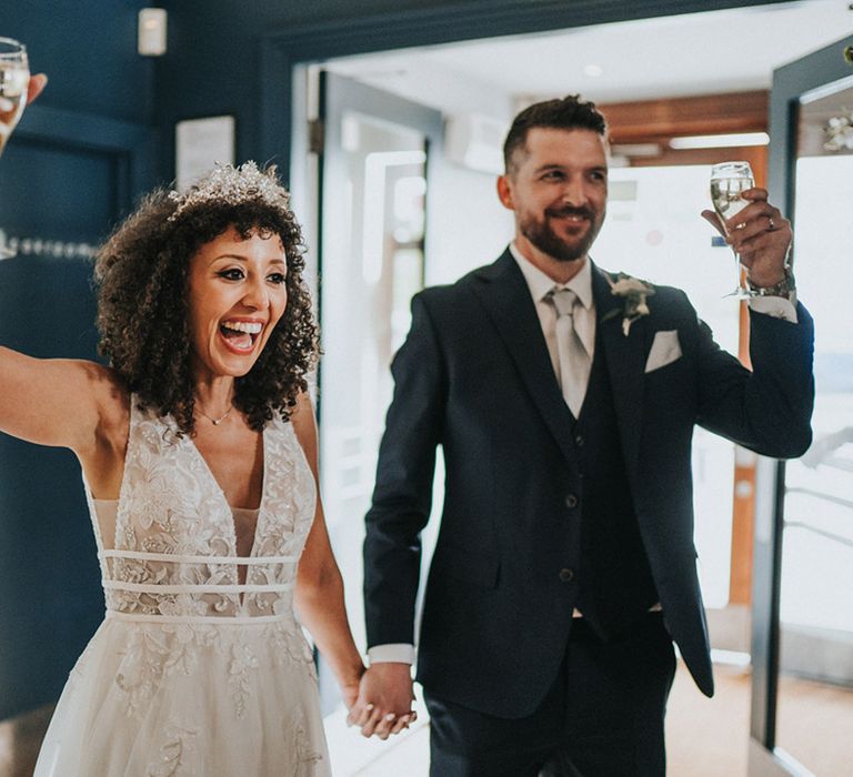 Bride in lace boho styled wedding dress lifts glass in the air alongside her groom