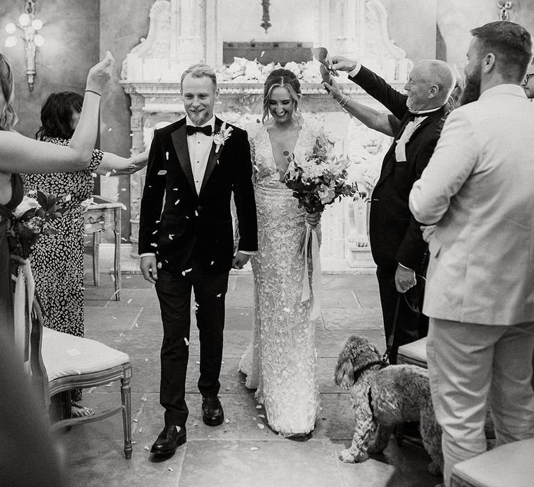 The bride and groom walk back down the aisle as a married couple as the wedding guests throw confetti over the couple 