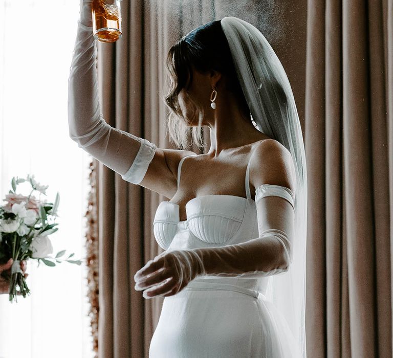 Bride on wedding morning spraying perfume with sheer gloves on 