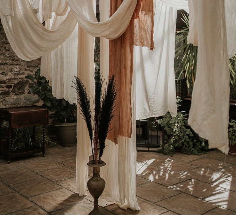 White, off-white and burnt orange wedding drapes decorations with tropical plants 