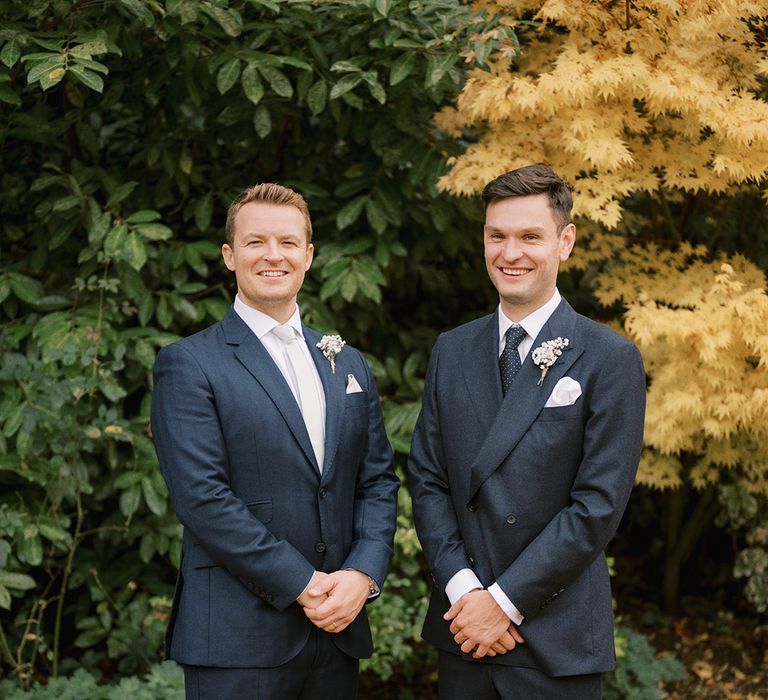 The groom in a dark blue double breasted suit with the best man in a matching colour suit jacket with white baby's breath buttonhole 