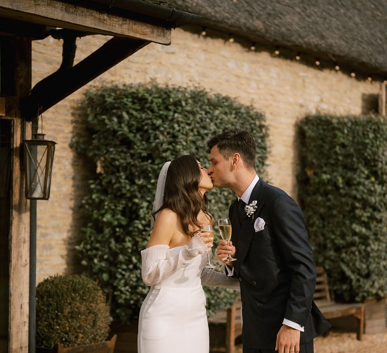 Bride in strapless wedding dress with pearl Jimmy Choo shoes and pearl veil kissing the groom in a dark suit for Oxfordshire wedding at The Tythe Barn