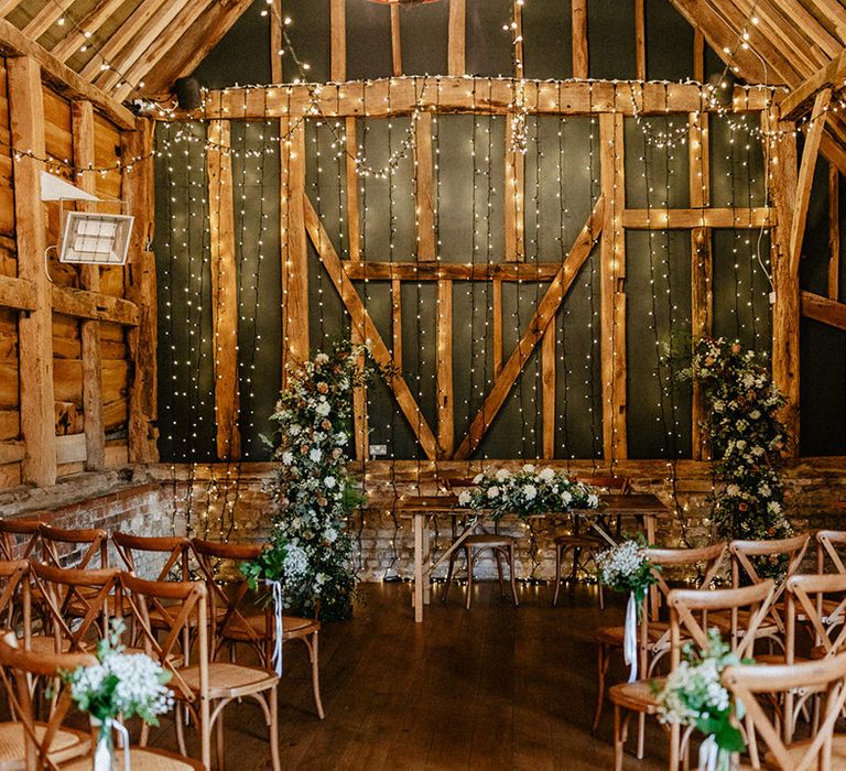 Rustic Silchester Farm wedding ceremony room decorated with flower column arrangements, fairy lights and simple gypsophila chair back decor