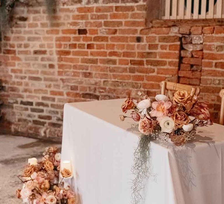 White tablecloth with dried blush garden rose, peony and dried flower arrangements and pillar candles in front of exposed brick at Lodge Farm wedding venue 