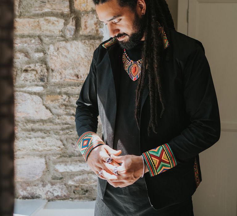 mixed Caribbean groom in a black outfit looking out the window 