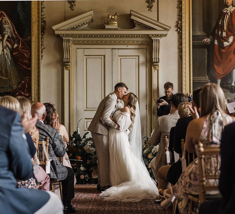 The bride and groom share their first kiss as a married couple after their wedding ceremony with the bride in a whimsical wedding dress and groom in houndstooth suit 