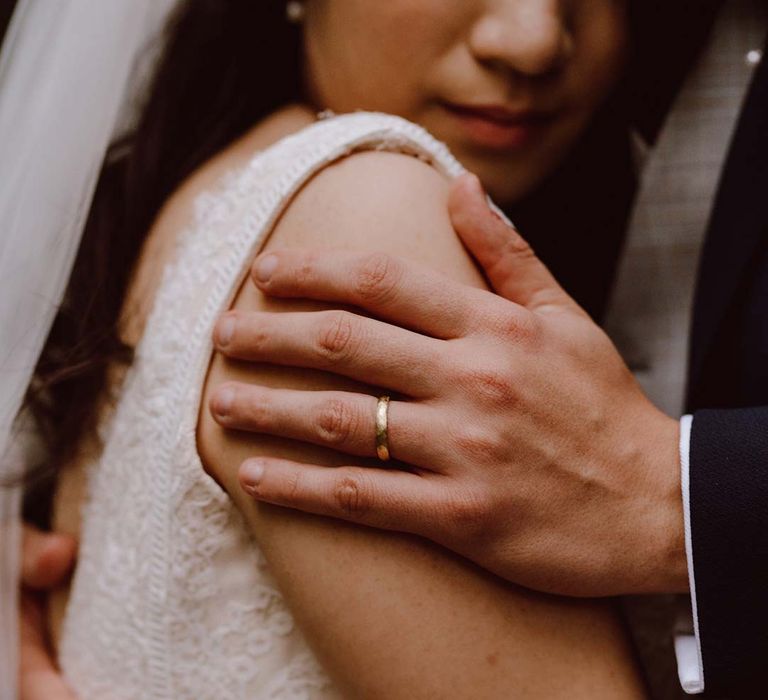 Wedding couples portraits - bride wearing red lace wedding dress and groom embracing her showing his golden wedding ring 