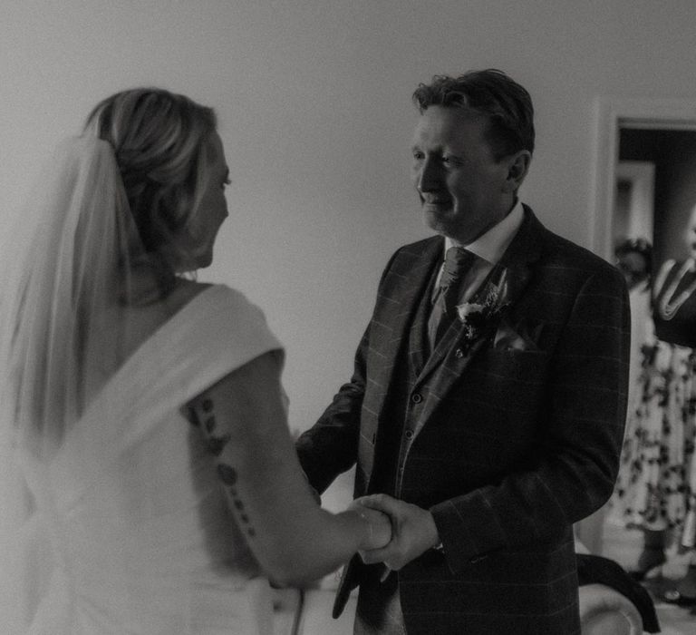 Bride in off the shoulder wedding dress standing with father of the bride in three piece textured suit 