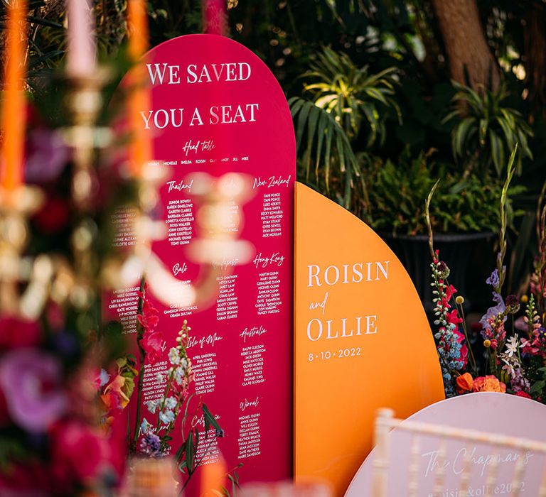 A bright pink arched seating chart with orange welcome sign at glass house wedding venue 