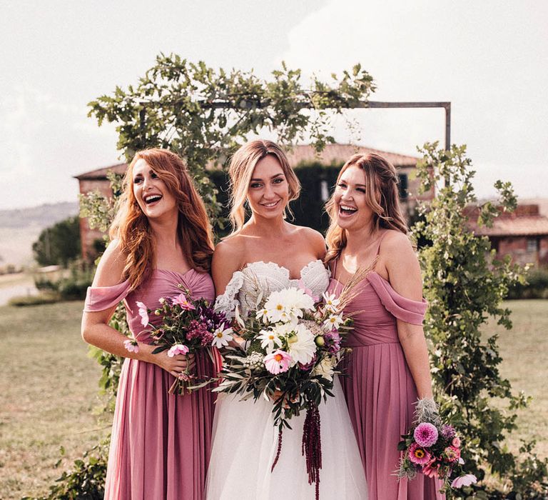 Pleated dark pink bridesmaid dress with off the shoulder detail with the bride in a Rue de Seine wedding dress 