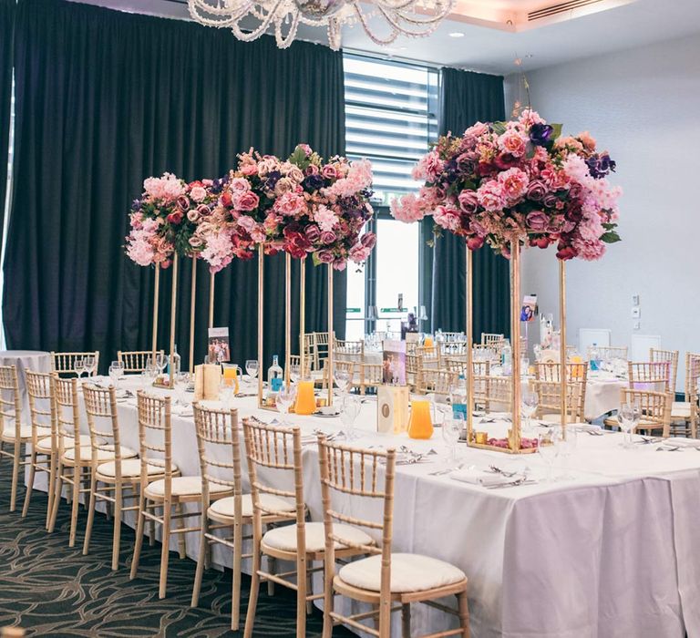 Templars Barn wedding reception room with large pink floral displays with pink azaleas, garden roses, rhododendrons and foliage on floral stands on classic wedding tablescape under large chandelier 