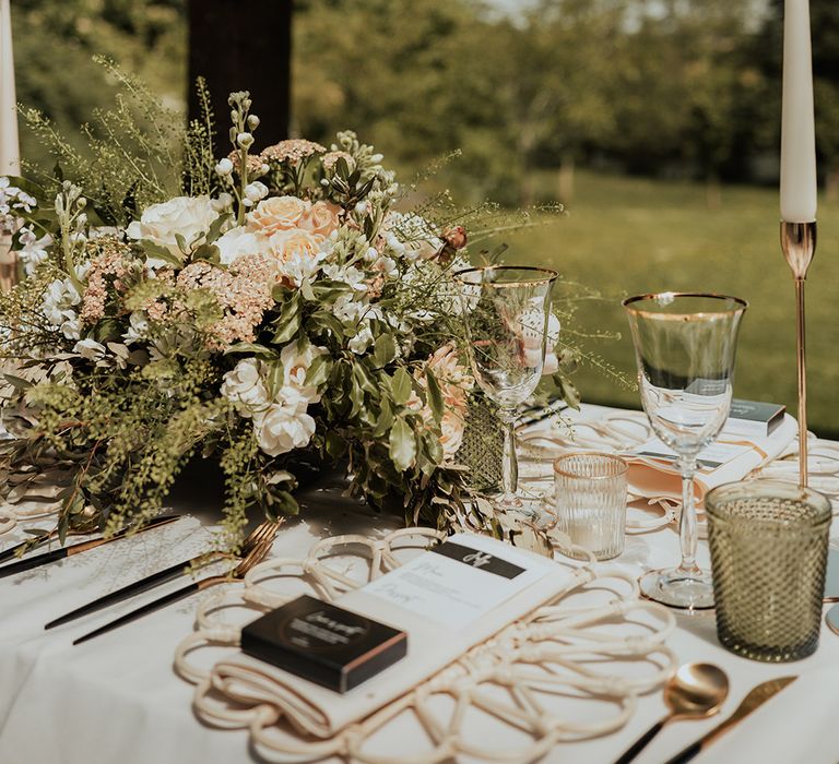 Pink and white flower arrangement decorating the table with white taper candles, a floral wicker placemat and black and white menu card 