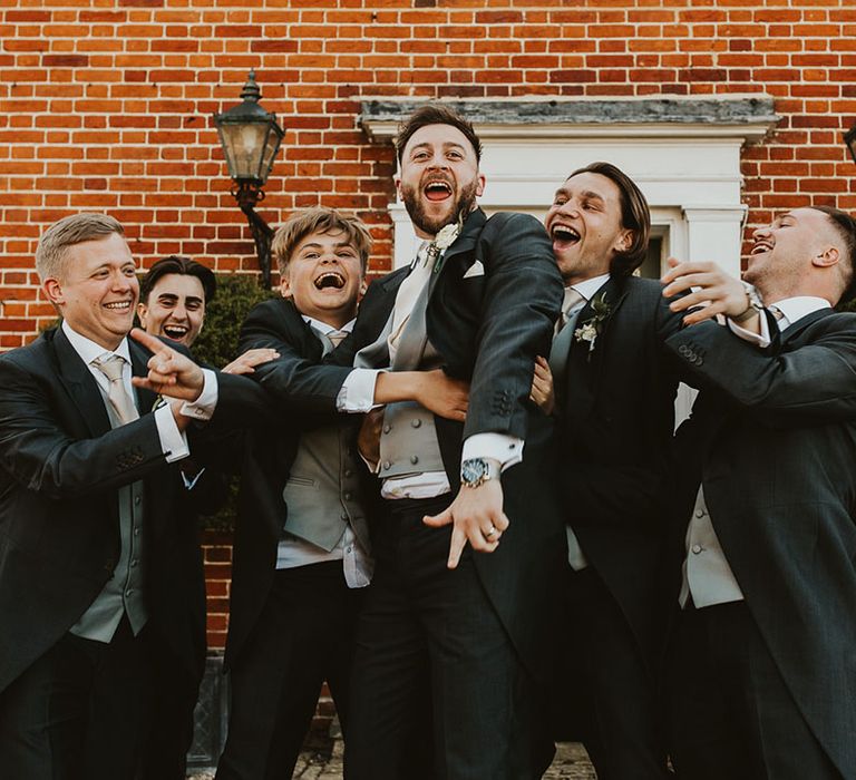 Groom and groomsmen having a laugh together wearing black and grey morning suits 