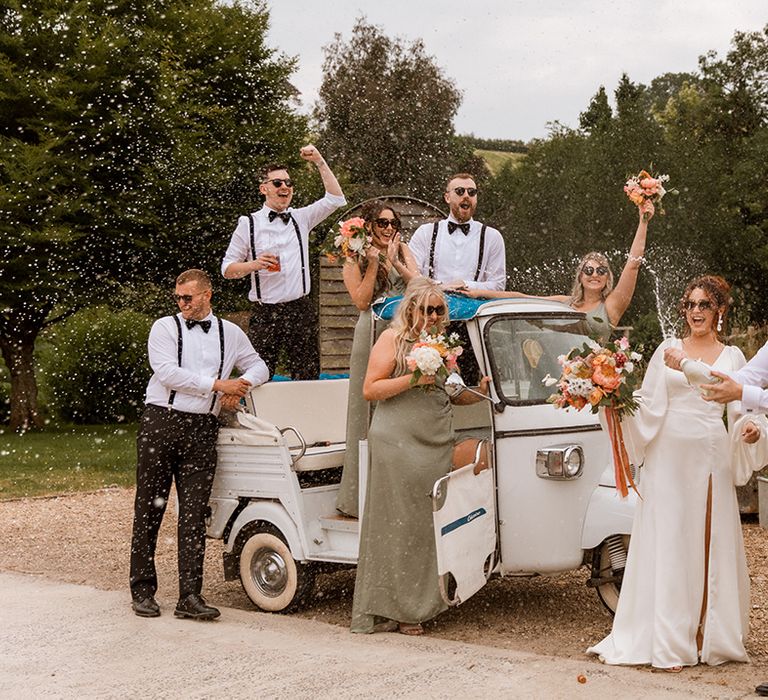 Champagne popping moment for the bride and groom with their wedding party in front of their tuk tuk wedding transport 