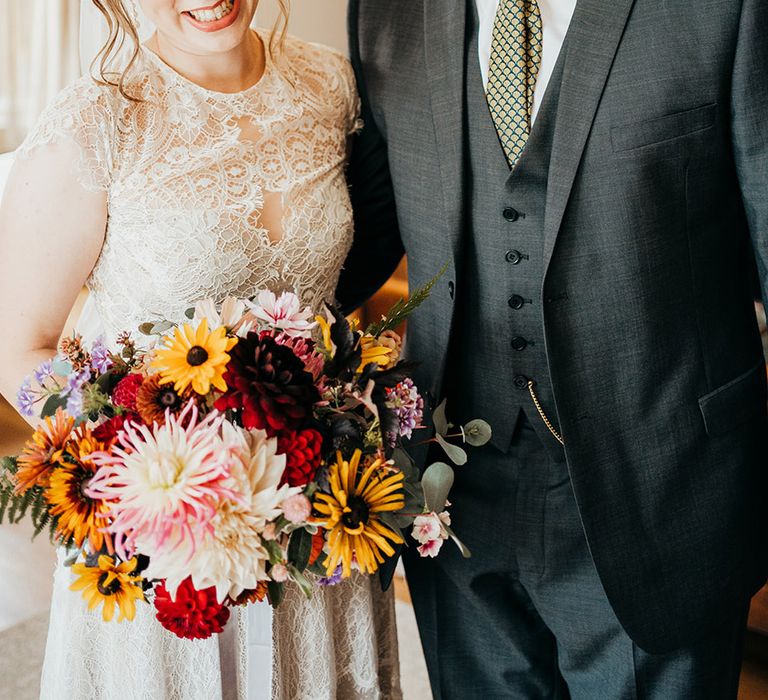 Bride carrying red and yellow autumnal seasonal bouquet with the father of the bride in a grey suit 