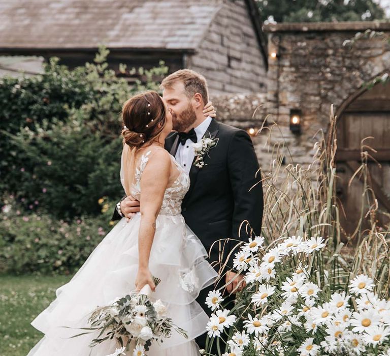 Romantic bride and groom portrait by flowerbed of daisies