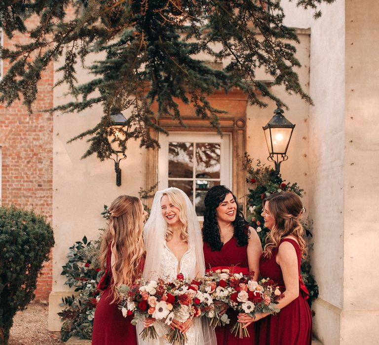 Bridal party wearing festive red bridesmaid dresses with the bride holding red rose bouquets 