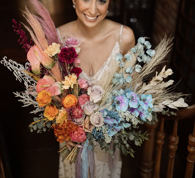 Bride with colourful eyeshadow holding orange and blue colourful wedding bouquet with pampas grass and more 