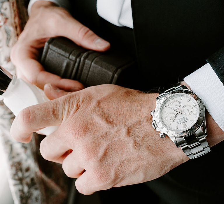 Groom wearing silver watch accessory holding a bottle of Creed cologne 