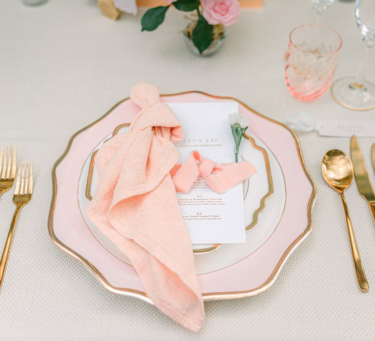 Peach theme wedding tablescape and place setting with wavy light pink plate with gold rim and peach napkin 