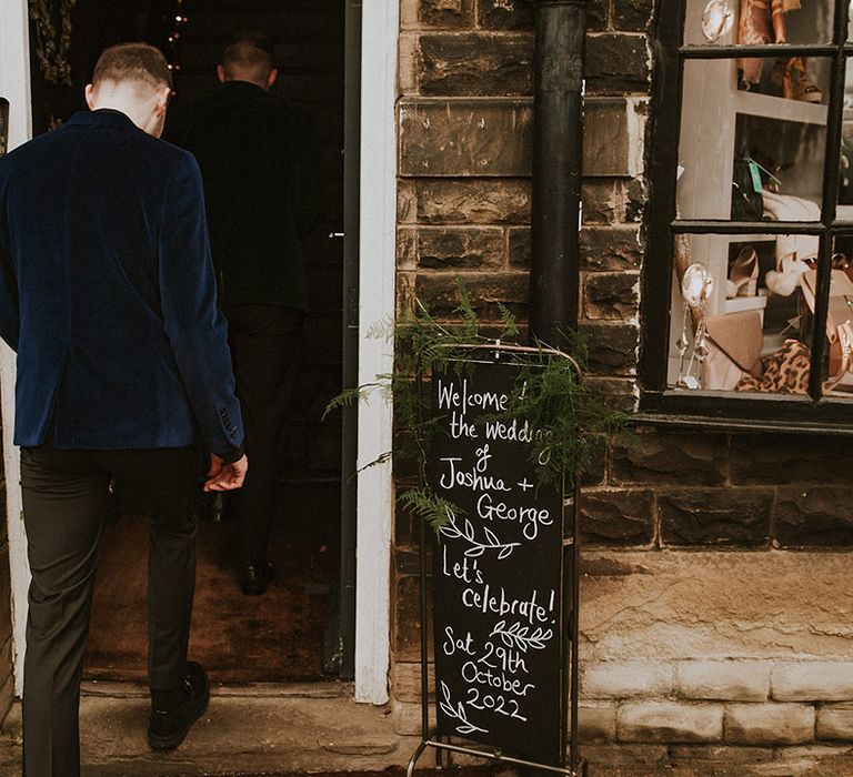 The groom wears a navy blue velvet suit jacket as he enters the wedding venue 