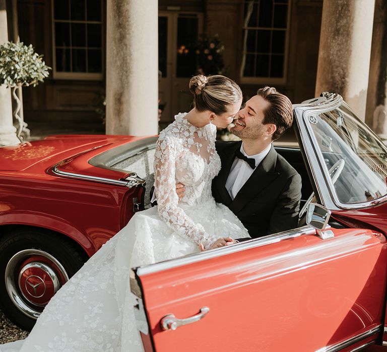 Bride and groom pose in the red wedding car for luxe country house wedding 