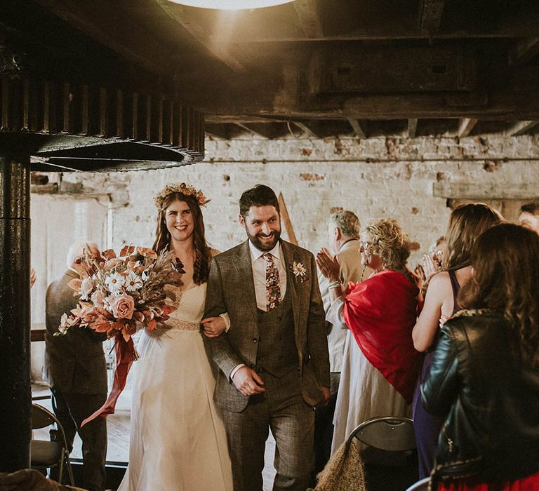 Bride and groom walking back down the aisle as a married couple with the bride wearing a flower crown carrying a dried flower boho bouquet