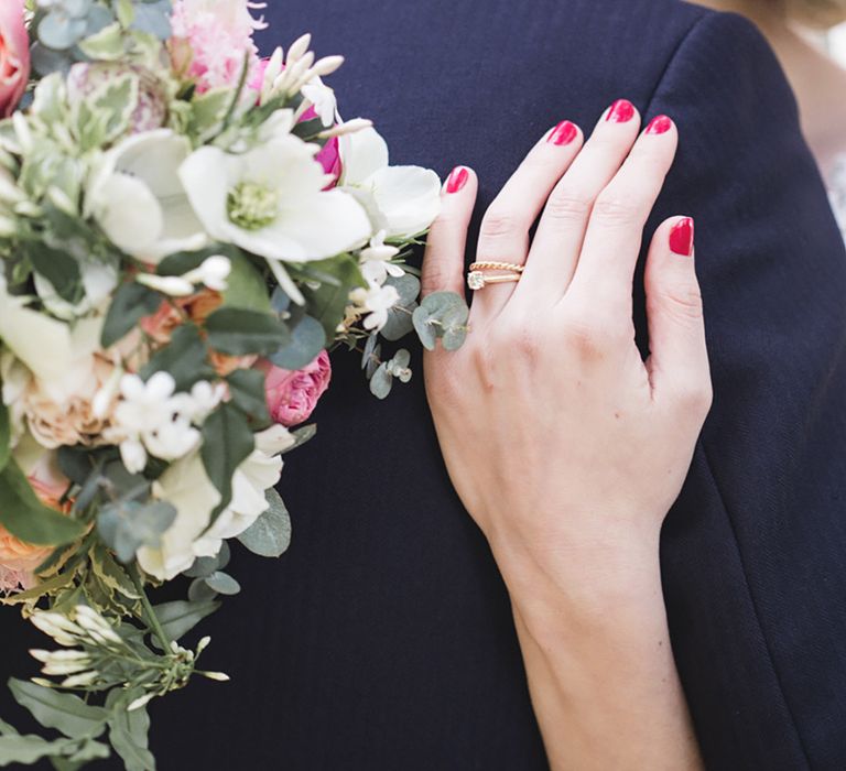 Bride wearing gold wedding and engagement ring with short rounded red nails 