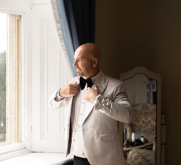 Groom getting ready for the wedding in a silvery grey suit jacket with black bow tie 