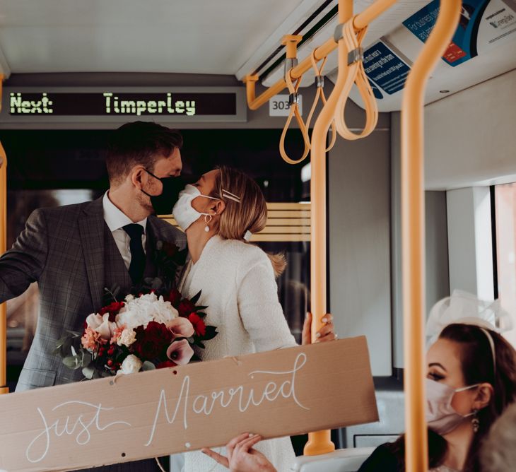 Bride and groom kissing on the tram holding a cardboard 'just married' wedding sign 