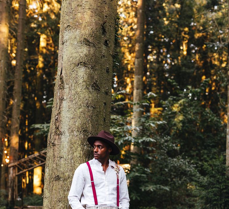 Groom poses outdoors in red braces and tartan trousers