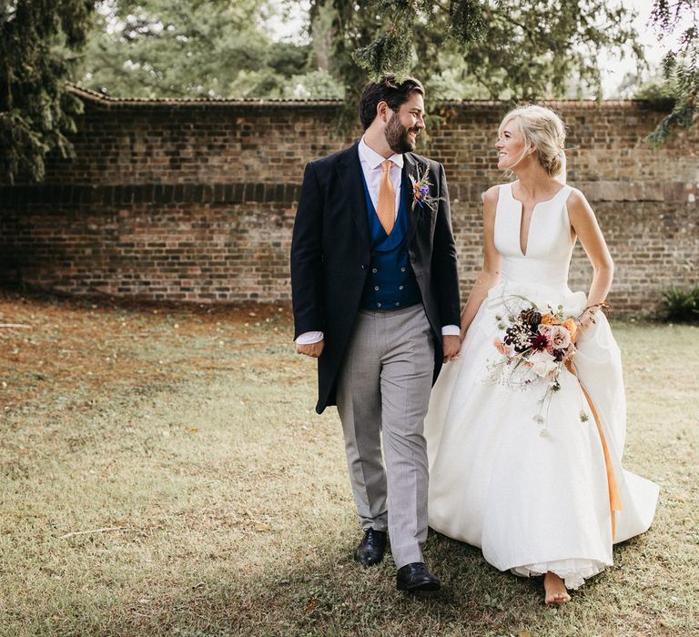 Bride and groom portrait with the groom in a morning suit with grey trousers, black jackets and blue horseshoe waist coat holding his brides hand in a Jesus Peiro wedding dress