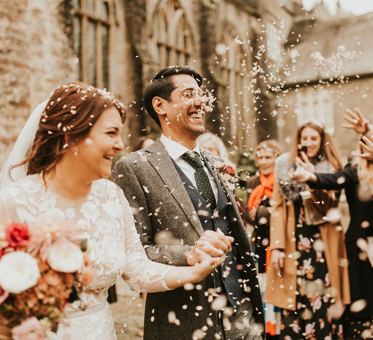 Confetti moment with groom in a grey and navy wool suit and waistcoat and the bride in a lace wedding dress with long sleeves 