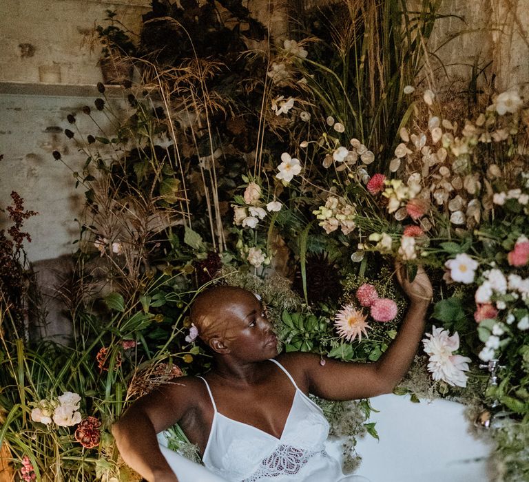 Bride with alopecia in a satin chamise sitting in a roll top bath on the wedding morning 