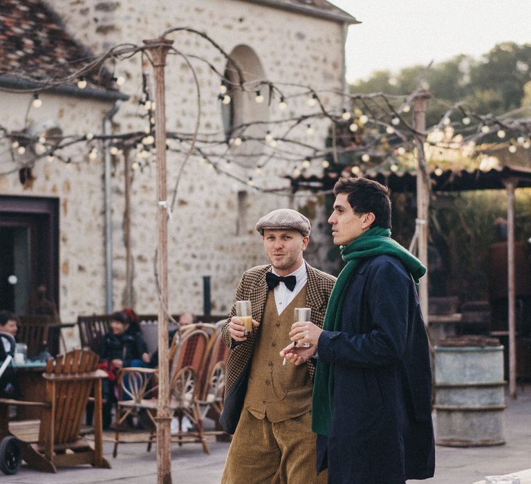 Wedding guest in Peaky Blinders outfit with cord trousers, wool waistcoat, bowtie, check overcoat and flat cap