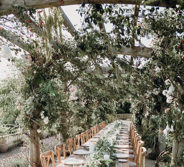 Rustic wooden wedding table with light wooden chairs and wedding table garland under canopy of foliage at Euridge Manor wedding