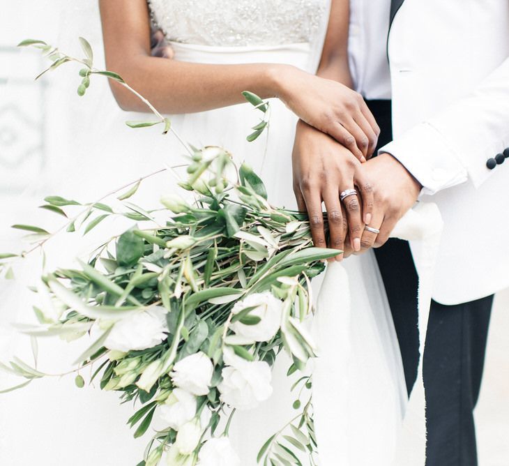 Bride & groom hold white floral bouquet with green foliage