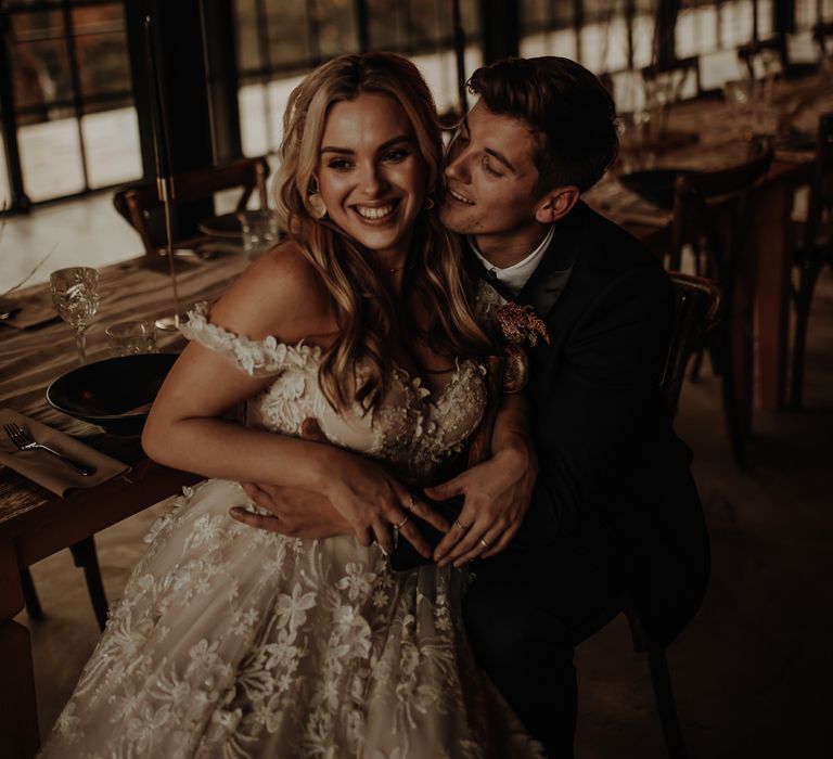 Groom sitting at the reception table with his bride on his knee in an appliqué wedding dress