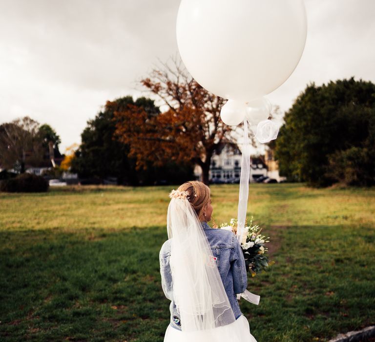 Bride wears personalised denim jacket whilst holding white balloon