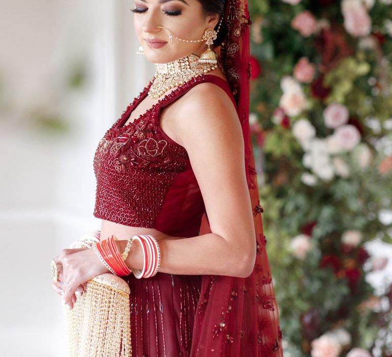 Bride stands wearing burgundy coloured outfit with golden jewellery 