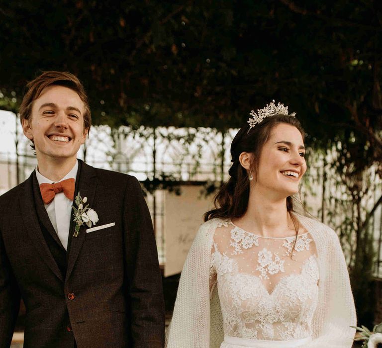 Bride and groom walking down the aisle in a black suit, lace dress and wool wrap 