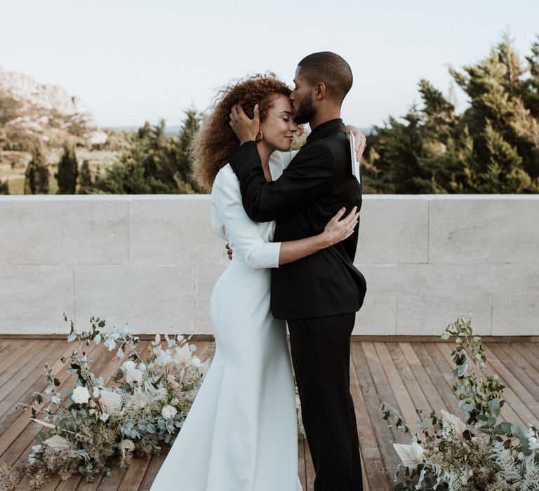 Bride and Groom embrace and Groom kisses Bride's forehead