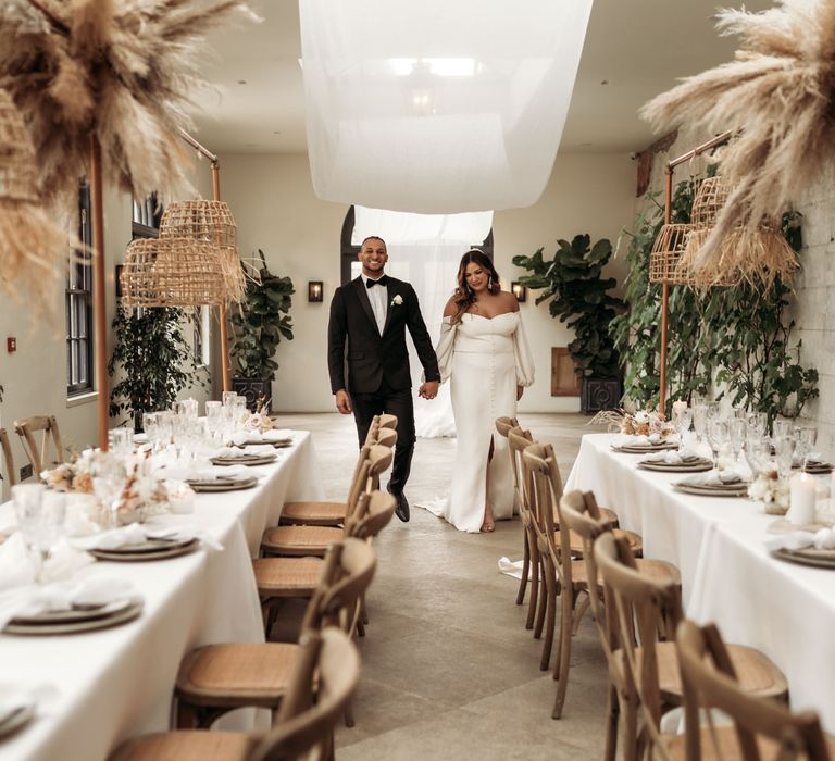 Bride and groom holding hands in The Fig House reception with earthy wedding decor and drapes 